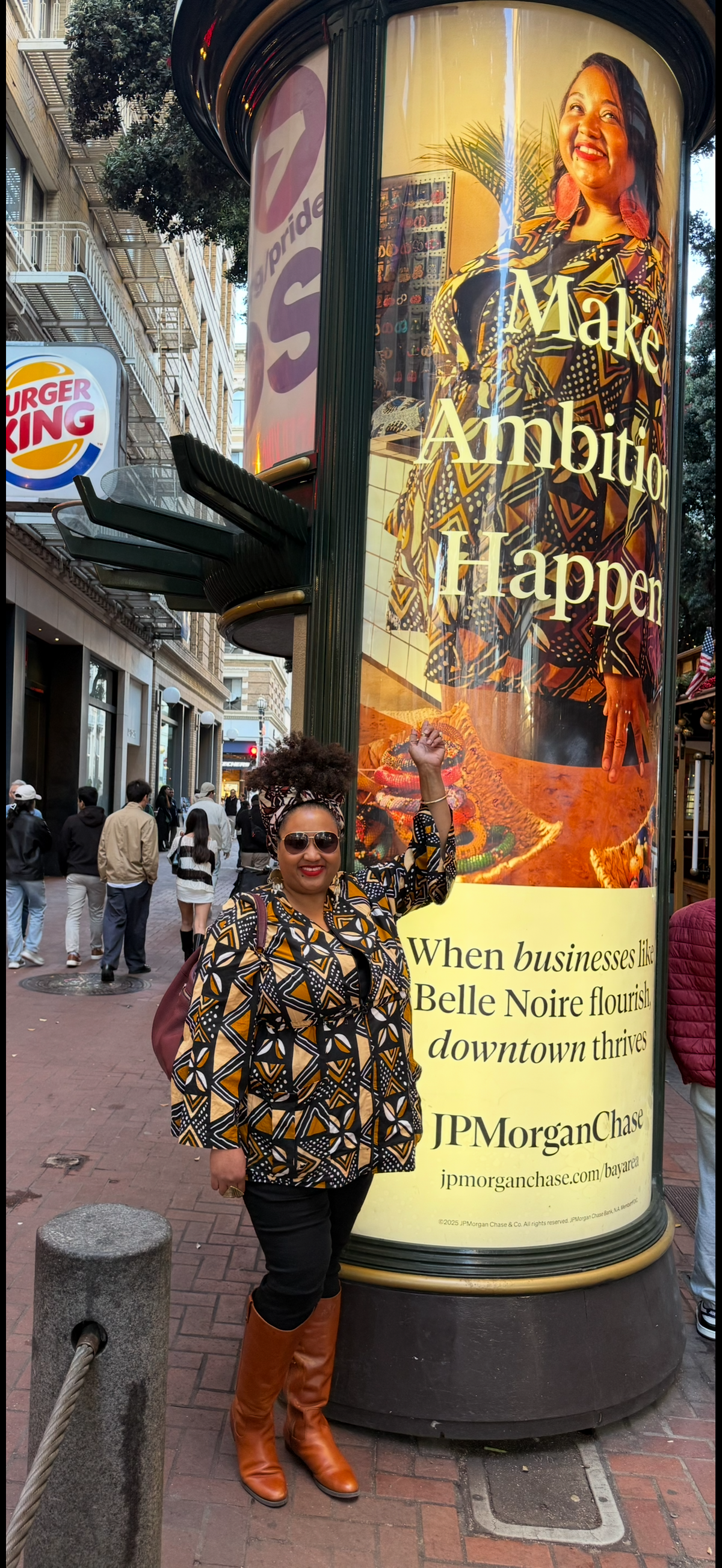 Nicole standing in front a street sign from JPMorganChase, advertising her business. The sign has a photo of Nicole and reads, "Make Ambition Happen."